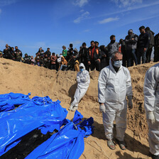 A number of men wearing white overalls and masks stand beside corpses in body bags on a beach in southern Gaza 