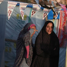 Two women stand under bunting hung up between tents in Gaza 