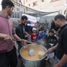 Three men serve food from a large pot to children in Gaza
