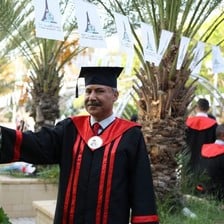 Dr. Abdel Nasser al-Saqqa in full graduation regalia, posing by palm trees. 