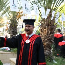 Dr. Abdel Nasser al-Saqqa in full graduation regalia, posing by palm trees. 