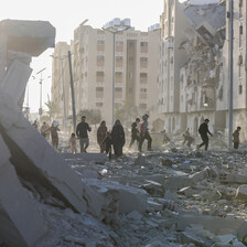 People walk in front of the husks of destroyed buildings