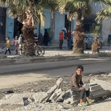 A boy sits on the side of a road, holding a pot. 