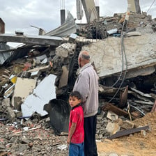 A boy and a man beside the remains of a building bombed by Israel 