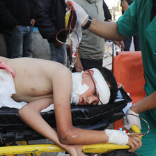 An injured young man with bandages on his body and head lies on his side