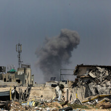 A plume of smoke rises from a horizon of destroyed buildings