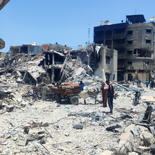 Two adults stand and one child sits down amid what remains of buildings that have been attacked in Gaza City 