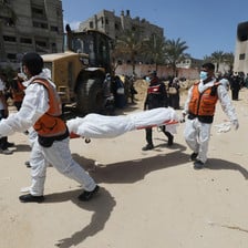 Men wearing masks and vests carry a body on a stretcher 