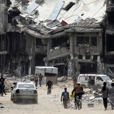 A collapsed building looms large as people walk down a street