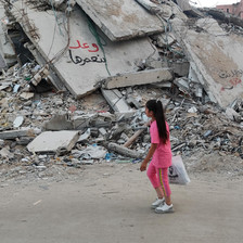 A girl walks past the remains of a building which has some graffiti written on it 
