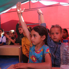 A few girls hold up their hands in a classroom inside a tent 