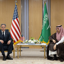 Two men sit flanked by the American and Saudi Arabian flags