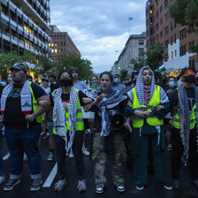 Students wearing checkered scarves and face masks link arms in a protest