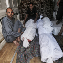 Two men sit beside corpses wrapped in shrouds 