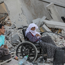 A woman in a wheelchair and a man sit in what remains of a building destroyed by Israel 