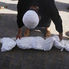 A man bends down to touch the shroud covering the body of a dead child