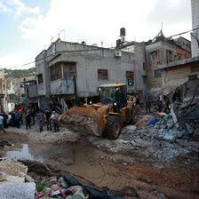 A bulldozer between buildings in a badly damaged Palestinian refugee camp