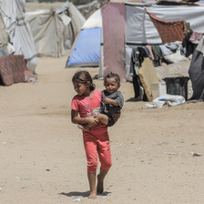 A child holds a smaller child beside a number of tents in Gaza 