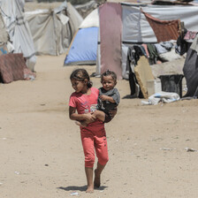 A child holds a smaller child beside a number of tents in Gaza 