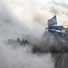 An Israeli tank in a cloud of smoke and dust flying an Israeli flag