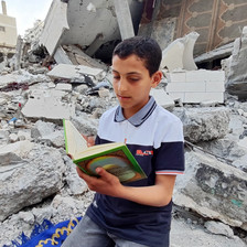 A boy reads a book amid the rubble of a house