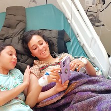 Two girls with a mobile phone lying on a hospital bed 