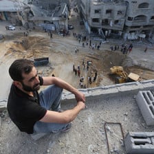 A man sits on a roof inspecting damage after airstrikes