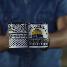 A man holds up two ceramic cups, one with the kefiyeh motif and one depicting al-Aqsa mosque in Jerusalem