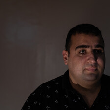 A man in a dimly lit room looks at the camera