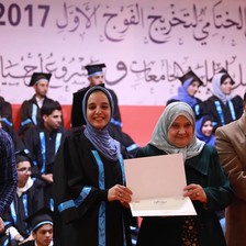 A young woman poses at a graduation ceremony holding her diploma