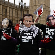 People wear masks showing the faces of politicians and T-shirts saying Stop Arming Israel and Ceasefire Now 