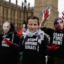 People wear masks showing the faces of politicians and T-shirts saying Stop Arming Israel and Ceasefire Now