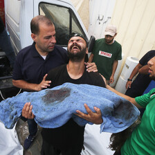 A man cries while tipping his head back and holding the shrouded body of a child