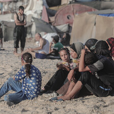 A family sit beside tents on a beach 