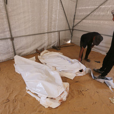 Two men stand beside a number of dead bodies wrapped in white shrouds 