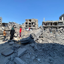 People beside an upturned car and rubble and the remains of buildings in Gaza 