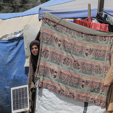 A woman peers out from behind a piece of cloth on a makeshift tent