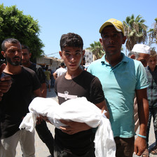 A young man carries a dead body wrapped in a white shroud 