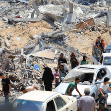 Heaps of rubble beside people walking and cars in southern Gaza 