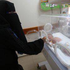 A woman reaches for a baby in a NICU