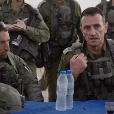 Hiram and Halevi in fatigues seated at table surrounded by armed soldiers