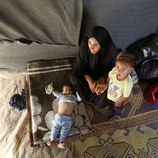 A woman sits on a rug on the ground with two little children