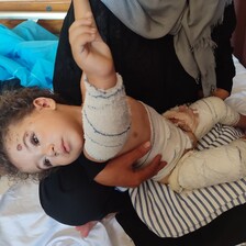 An injured child held by a woman sitting on a hospital bed 