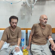 Two men sit on chairs in a hospital or a clinic 