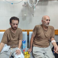 Two men sit on chairs in a hospital or a clinic