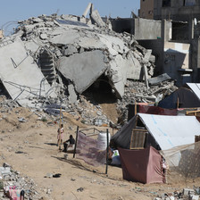A homemade tent stands next to a destroyed building
