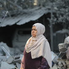 A woman stands in front of the rubble of a house