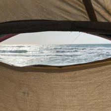 A slit from a white tent looks out onto a sliver of ocean view