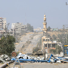 A daytime view of a street with ruins of buildings and an Israeli tank. 