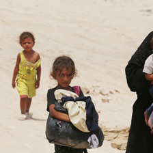 A woman holds a baby while two other children walk beside or behind her 